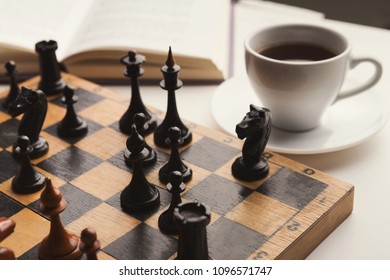 Wooden desk with chess play, book and cup of coffee on white table. Board game, intelligence and brain upgrade concept