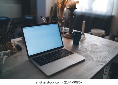 Wooden Desk With Cup, Opened Laptop Computer And Many Art Objects And Equipment In Dark Art Studio With Sunny Lighting. Working Place Of Artist, Sculptor Or Other Art Worker. No People