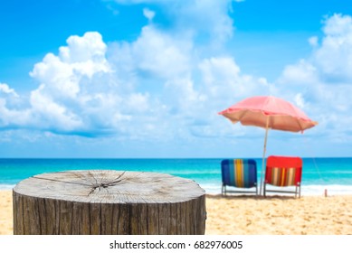 Holzschreibtisch oder Stumpf am Sandstrand im Sommer, Liegestühle mit Regenschirm.