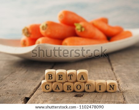 Wooden dices with the German words beta carotene and fresh carrots in the back, healthy eating concept