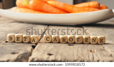 Wooden dices with the words beta carotene and fresh carrots in the back, healthy eating concept