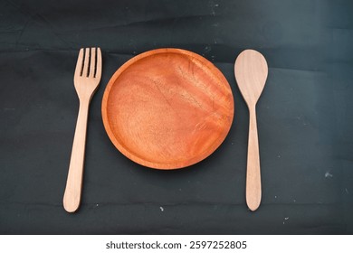 Wooden dining set featuring a plate, fork, and spoon on a dark canvas backdrop, showcasing sustainable kitchenware.