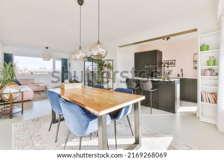 Wooden dining table under pendant lamp in open plan kitchen with living room