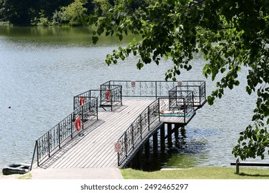 Wooden Dock With Black Railings Extending Over a Calm Lake on a Sunny Day - Powered by Shutterstock