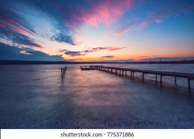 Wooden Dock And Fishing Boat At The Lake, City Lights At Sunset