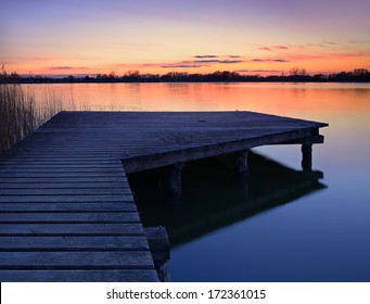 Wooden Dock On Calm Lake At Sunset