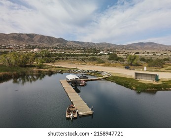 A wooden dock on the Lake Palmdale surrounded by mountains against a cloudy sky