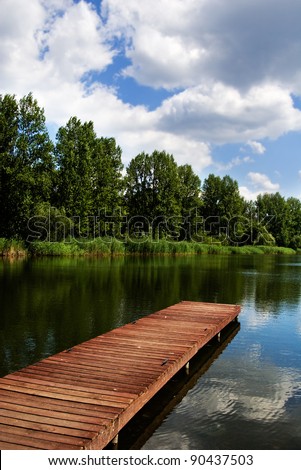 A wooden dock, pier, on a lake in summer sunny day, blue sky, white clouds, lake