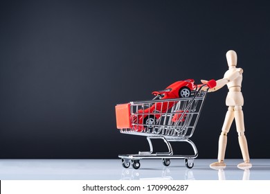 A wooden doll carries a red car model in metal shopping cart. Man buy his new car in dealership. Concept of buying new cars, moneys, miniature. Stay on gray background. - Powered by Shutterstock