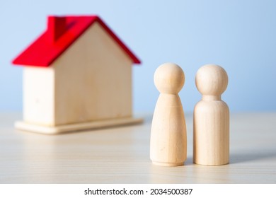 Wooden Doll Family Stands In Front Of House Model.