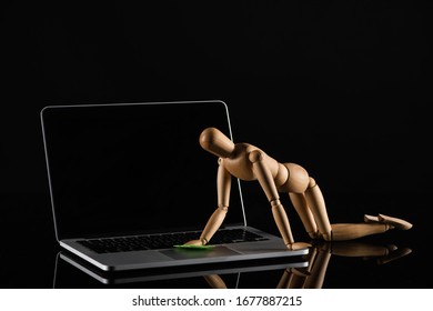 Wooden doll on all four position imitating dusting laptop on black background - Powered by Shutterstock