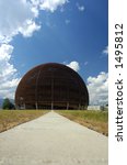 A wooden dome (the Globe of Science and Innovation at the European particle research laboratory CERN, Switzerland) rises against a blue sky with a few cumulus clouds.