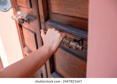 A wooden door and a hand on a massive metal handle. A woman's hand opens or closes the door. Close-up photo. - Powered by Shutterstock