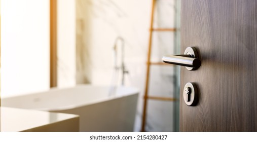 wooden door open to nice modern bathroom, marble walls. selective focus to door handle, bathroom and bathtub blurred on background