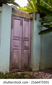 Wooden door without house. Door in a wall or fence overgrown by green lush tropical vegetation. A front door instead of a garden gate, land demarcation in Malaysian. Seen in Langkawi, Malaysia