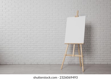 Wooden easel with blank canvas near white brick wall indoors. Space for text - Powered by Shutterstock