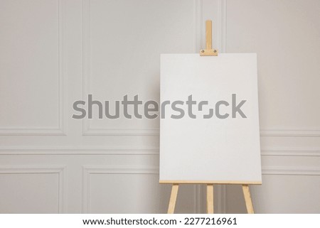 Wooden easel with blank canvas near white wall. Space for text