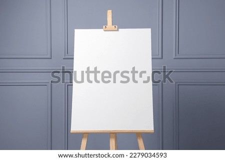 Wooden easel with blank canvas near grey wall indoors, closeup. Space for text