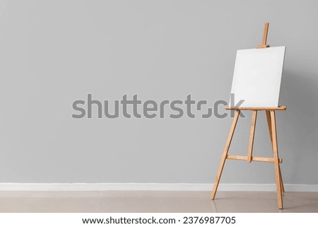 Wooden easel with blank canvas near grey wall