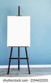 Wooden Easel With Blank Canvas On Light Blue Wall Background For Mockup Design. Space For Text