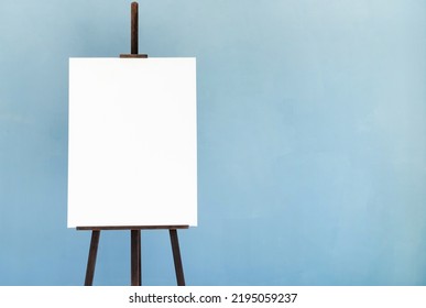 Wooden Easel With Blank Canvas On Light Blue Wall Background For Mockup Design. Space For Text