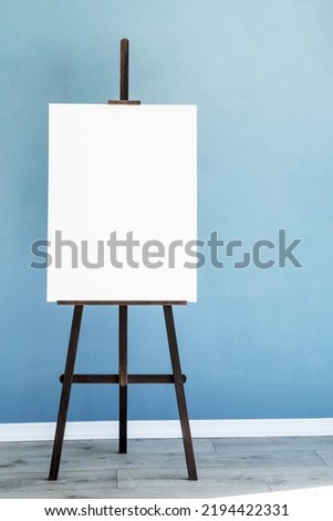 Wooden easel with blank canvas on light blue wall background for mockup design. Space for text
