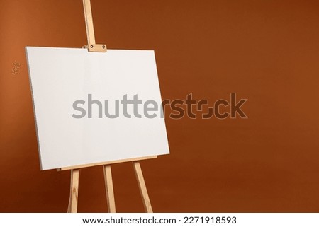 Wooden easel with blank canvas on brown background. Space for text