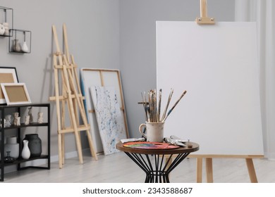 Wooden easel with canvas near paints, palette and brushes in artist's studio, space for text - Powered by Shutterstock