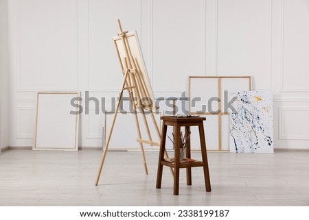 Wooden easel with canvas and painting supplies in artist's studio