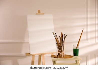 Wooden easel with empty canvas and brushes in art studio - Powered by Shutterstock