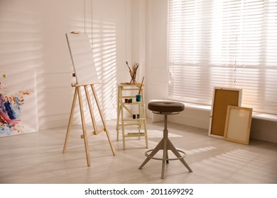 Wooden easel with empty canvas and stool in art studio