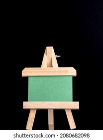 A Wooden Easel With Green Board And Dark Or Black Background. 