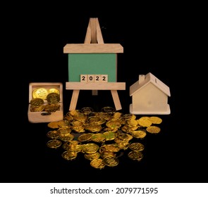 A Wooden Easel With Green Board And Numeric 2022 Simulating Welcoming New Year. Wooden Treasure Chest Filled With Coins Overflow On Floor And House Bank Representing Savings And Economic Concept