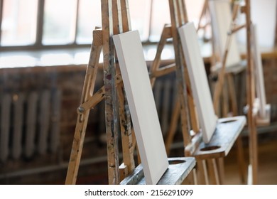 Wooden Easels With White Blank Canvas In Row Inside Cozy Loft Room, No People. Academy Of Art Education, Hobby, Training In Group Class For Creative Skill Development, Artistic School Tuition Concept