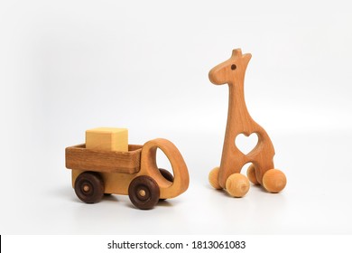 Wooden Eco-friendly Toy Giraffe On Wheels And A Truck With A Cube In The Back On A White Background, Place For Text