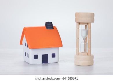 Wooden Egg Timer Or Hourglass With Running Sand Measuring Passing Time To A Deadline Alongside A Model House In A Conceptual Image