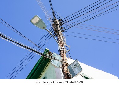Wooden electric pole with many attached wires, cables and LED street lantern on a blue sky background