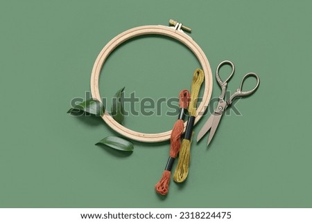 Wooden embroidery hoop with mouline threads, scissors and leaves on dark green background