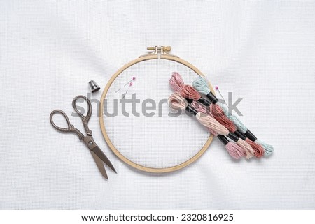 Wooden embroidery hoop with mouline threads, scissors and canvas as background