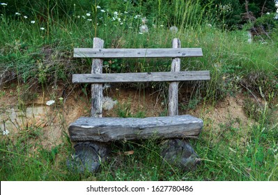 Wooden empty bench in the forest. Rustic bench and fresh green grass near it. Homemade bench made of wooden logs near a forest path. Resting seat while hiking.