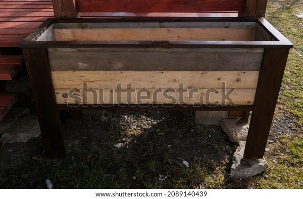 Wooden empty raised planter box  in front of a\
patio, build from recycled material\
.