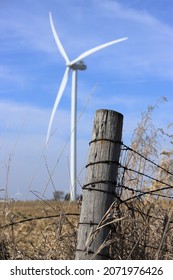 Wooden Farm Fence Post With Large Wind Turbine In Background And Blue Skies