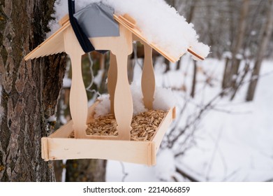 Wooden Feeder For Wild Forest Birds With Food Hanging On Tree Covered With Fresh Icy Frozen Snow And Snowflakes On Frosty Winter Day In Forest Or Garden. Animal Care. Snowy Winter Season In Nature