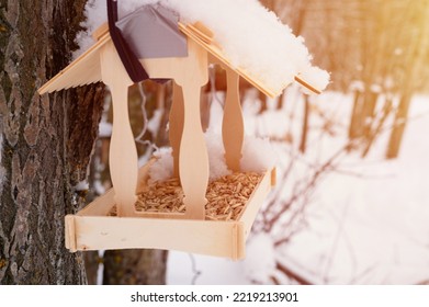 Wooden Feeder For Wild Forest Birds With Food Hanging On Tree Covered With Fresh Frozen Snow And Snowflakes On Frosty Winter Day In Forest Or Garden. Animal Care. Snowy Winter Season In Nature. Flare