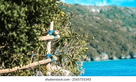 A wooden fence with blue rope ties is on a hillside overlooking a body of water. The scene is peaceful and serene, with the blue water and green trees creating a calming atmosphere - Powered by Shutterstock