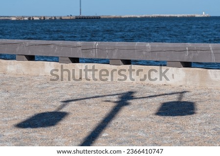 A wooden fence and a light pavement, on which the shadow of a lantern. Mobile floating platform in the sea and clear blue sky in the background. Copy space. Background for quotes.