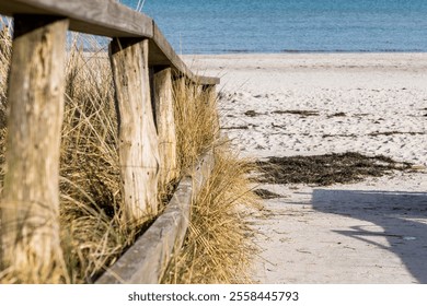 A wooden fence is on the Baltic Sea beach. The fence is old and weathered. The beach is sandy and the water is blue in Germany - Powered by Shutterstock