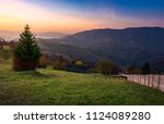 wooden fence on a grassy rural hillside at autumn dawn. horese, woodshed and spruce in the scene. gorgeous landscape in forested mountains with red foliage