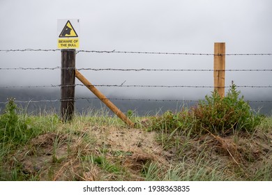 Wooden fence with wire. Sign beware of the bull, mountains covered with clouds in the background. Farming industry.