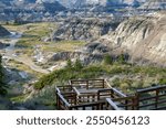 Wooden fenced boardwalk with a viewpoint to eroded sandstone formations on the hills of the canyon with unique flora growing in summer. Horseshoe canyon, Drumheller, Alberta, Canada.